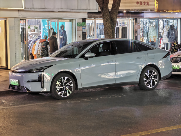 Elektrischer Mitsubishi Lancer EV auf einer nächtlich beleuchteten Stadtstraße geparkt, umgeben von erleuchteten Gebäuden, Schaufenstern, Schaufensterpuppen in Kleidern und Werbetafeln.