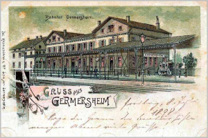 Alte Postkarte zeigt einen Bahnhofsbau in Deutschland mit einem Gebäude, einem Zaun, Menschen, Fahrzeugen, Bäumen und einem bewölkten Himmel; Text lautet "Bahnhof Germersheim".