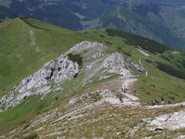 Gruppe von Menschen beim Wandern auf einem Berghang mit saftigem Grün und felsigem Gelände, Himmel im Hintergrund sichtbar