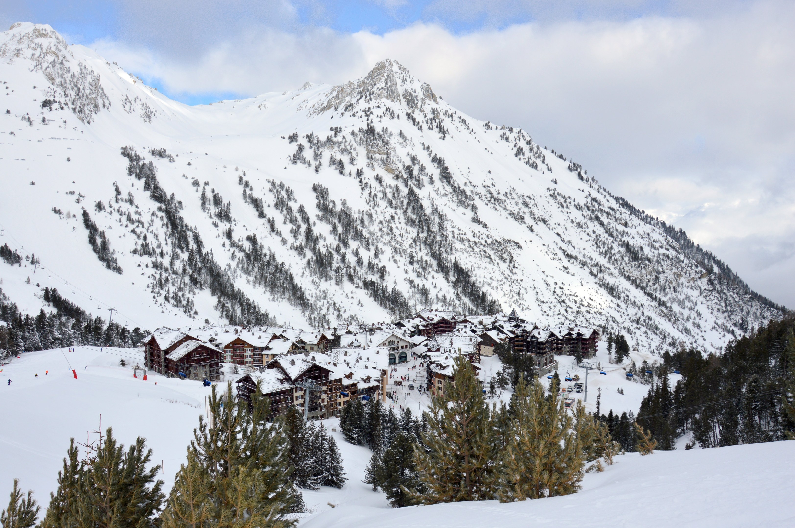 Winterszene eines Skigebiets mit schneebedeckten Bergen, schneebeladenen Bäumen, einer Skihütte zwischen den Bäumen und bewölktem Himmel.