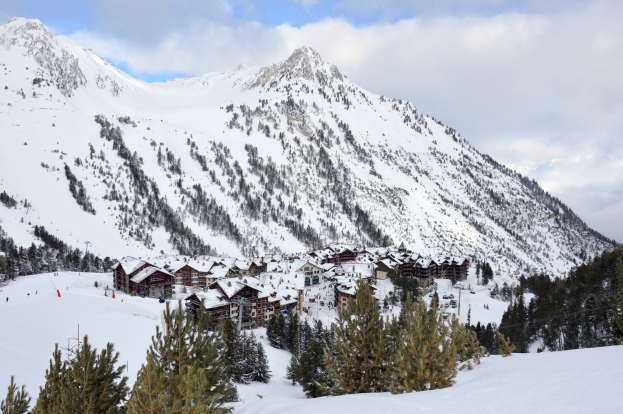 Winterszene eines Skigebiets mit schneebedeckten Bergen, schneebeladenen Bäumen, einer Skihütte zwischen den Bäumen und bewölktem Himmel.