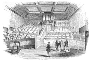Ein Schwarz-Weiß-Zeichnung eines großen viktorianischen Theaterauditoriums in London, England, gefüllt mit Menschen, Stühlen, Treppen, Geländern, Wänden, Fenstern und einem Dach.
