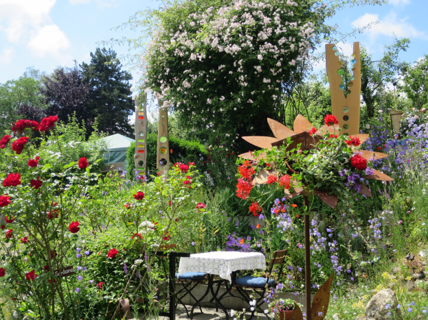 Ein Garten mit bunten Blumen und Pflanzen, der einen Tisch mit einer Decke und Stühlen zeigt, vor einem Baum und einem bewölkten Himmel auf dem Chelsea Flower Show.