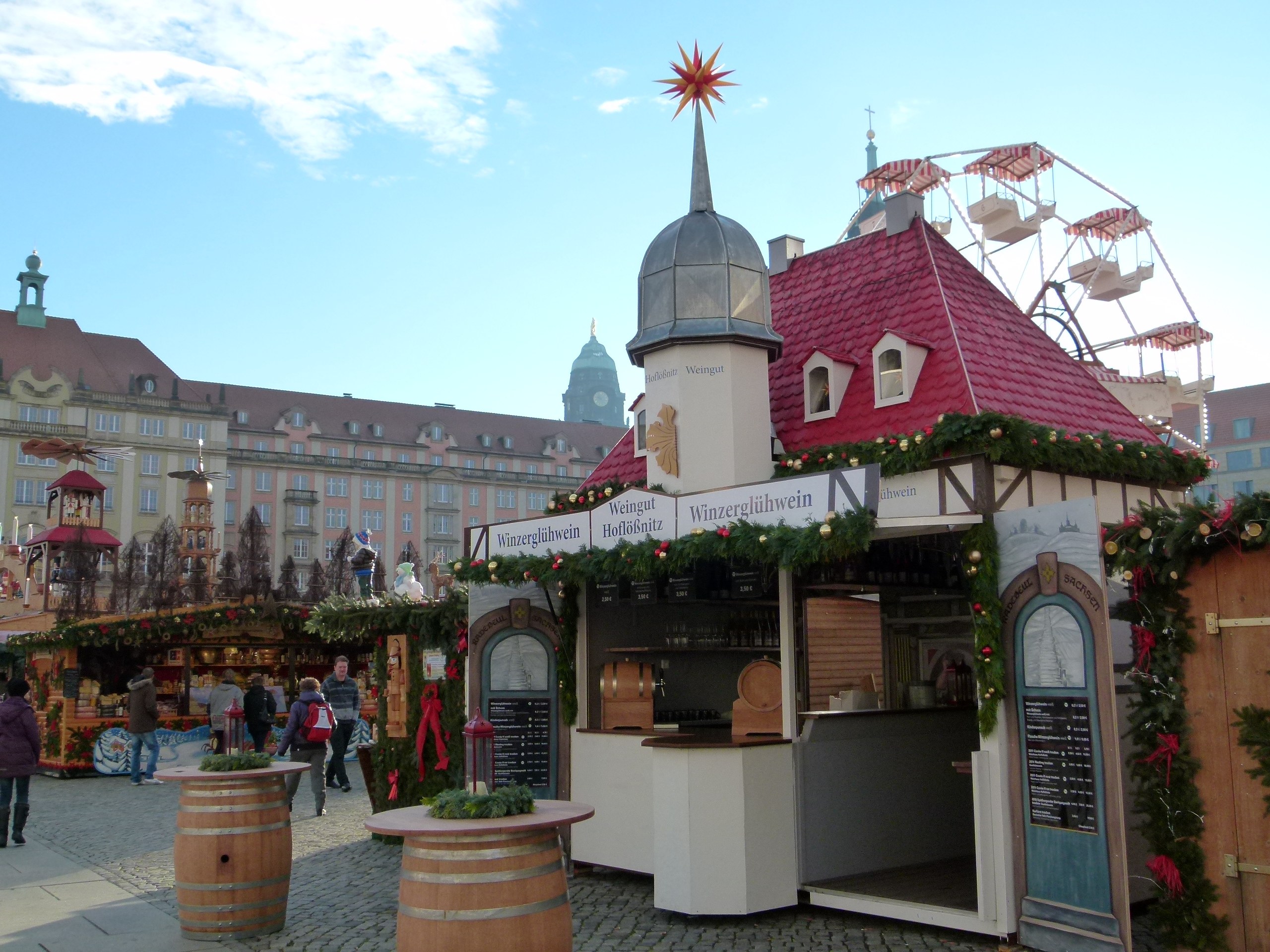Ein lebhafter Weihnachtsmarkt in Nürnberg, Deutschland, mit Menschen um geschmückte Stände, festlicher Beleuchtung, einem Riesenrad im Hintergrund und einer Tafel mit Schrift auf der rechten Seite.