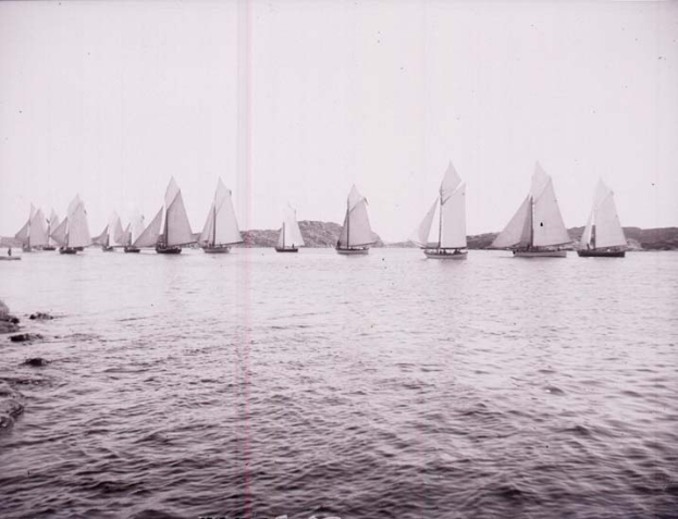 Schwarzes und weißes Foto von Segelbooten auf dem Wasser mit Hügeln und klarem Himmel, beschriftet als New York Yacht Club.
