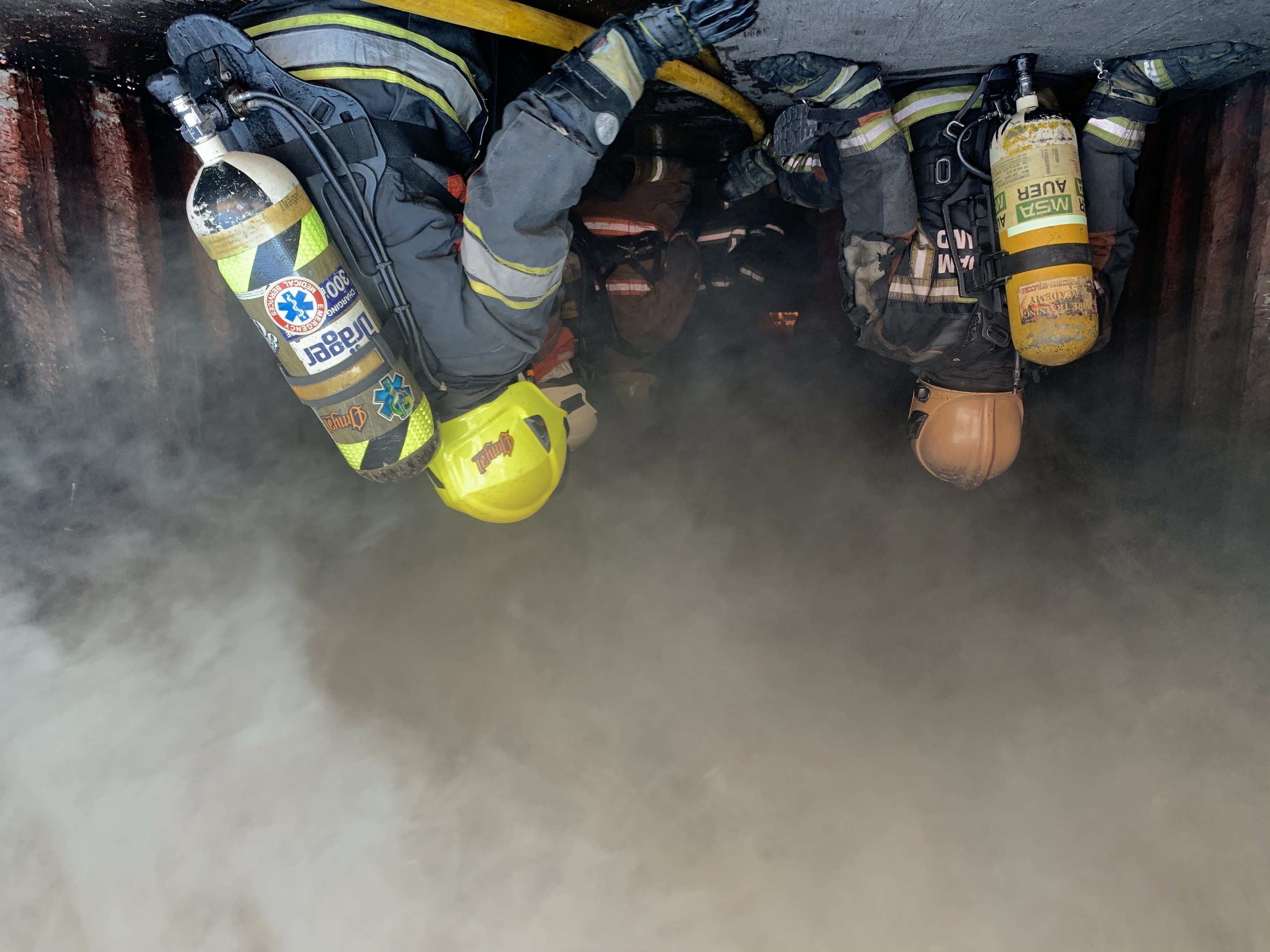 Feuerwehrleute in Schutzausrütstütndung arbeiten daran, ein Tunnelbrand zu löschen, mit Rauch, der von unten aufsteigt.