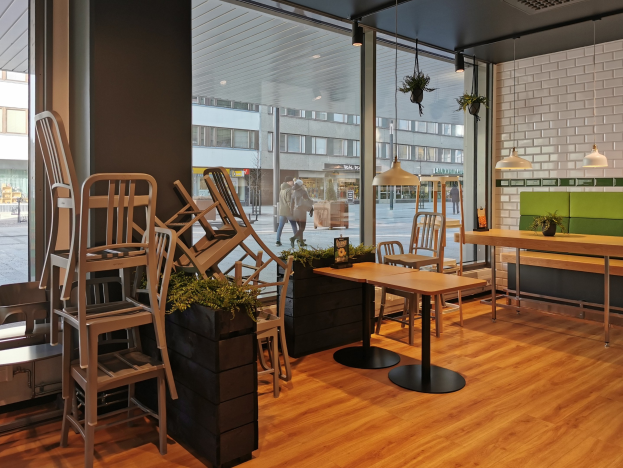 Ein Restaurant-Innenraum mit Holztischen und -stühlen in der Nähe eines großen Fensters, das eine städtische StraßenSzene in Berlin, Deutschland, zeigt.