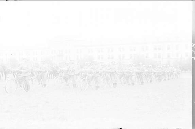 Schwarzes und weißes Foto von Radrennern im Schnee an einem Gebäude vorbei.