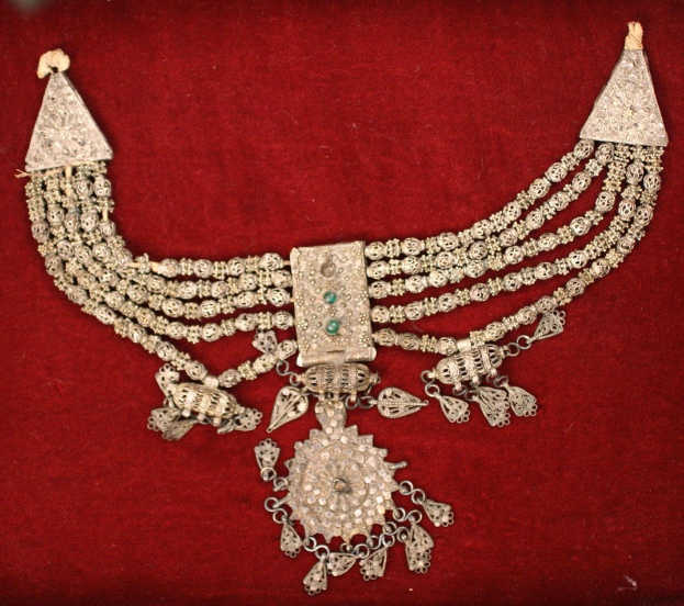 Silberne Kette mit Smaragden und Diamanten auf einem maronenfarbenen Samtgrund.