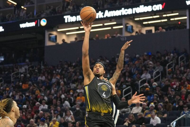 Ein Basketballspieler in einem schwarzen und gelben "Golden State Warriors"-Trikot wirft den Ball in einem vollen, hell erleuchteten Stadion.