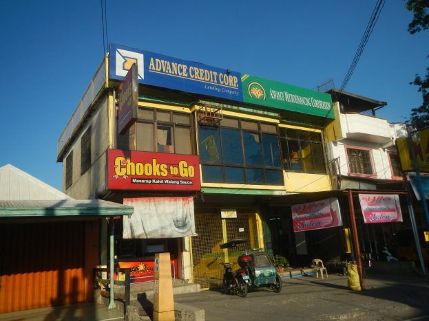 Ein Geschäftsgebäude mit einem "Advance Credit Corp"-Schild, umgeben von Fahrzeugen, Straßenschildern, Strommasten, Bäumen und einem klaren Himmel.