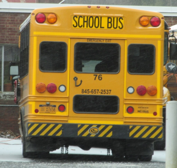 Ein gelber Schulbus steht vor einem Backsteingebäude mit Fenstern.