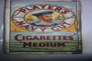 Ein Vintage-Plakat mit einer strengen Person in einer marineblauen Uniform, weißem Hemd und roter Krawatte, die Arme verschränkt, bewirbt "Player's Navy Cut Cigarettes Medium" in fetter schwarzer Schrift auf einem weißen Hintergrund.