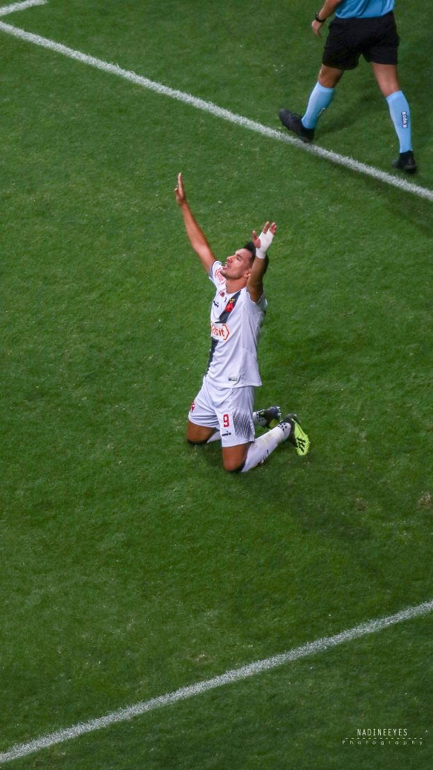 Ein Fußballspieler kniend auf dem Boden mit ausgestreckten Armen in Feierlaune, der einen Sportanzug und Fußballschuhe trägt.