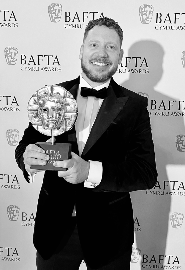 Ein Mann in einem Smoking, der eine BAFTA-Auszeichnung hält und lächelt, mit einem Hintergrund, auf dem "BAFTA Awards 2018" steht.