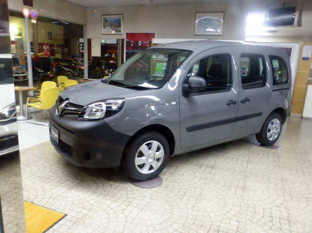 Ein Citroën Berlingo Multispace 1.6 HDI 90CV Feel Wagen steht auf einem Boden umgeben von verschiedenen Gegenständen wie Stühlen, Tischen, Schildern, einem Fernseher, einer Tür, einer Wand mit Fotorahmen und einer Decke mit Deckenleuchten.