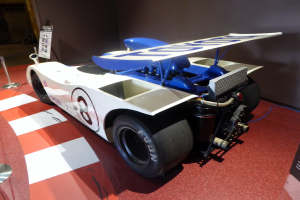 Ein weiß-blauer Rennwagen in einem Museum ausgestellt, umgeben von Absperrungen und Schautafeln, mit einer Wand im Hintergrund, die auf das Goodwood Festival of Speed hindeutet.