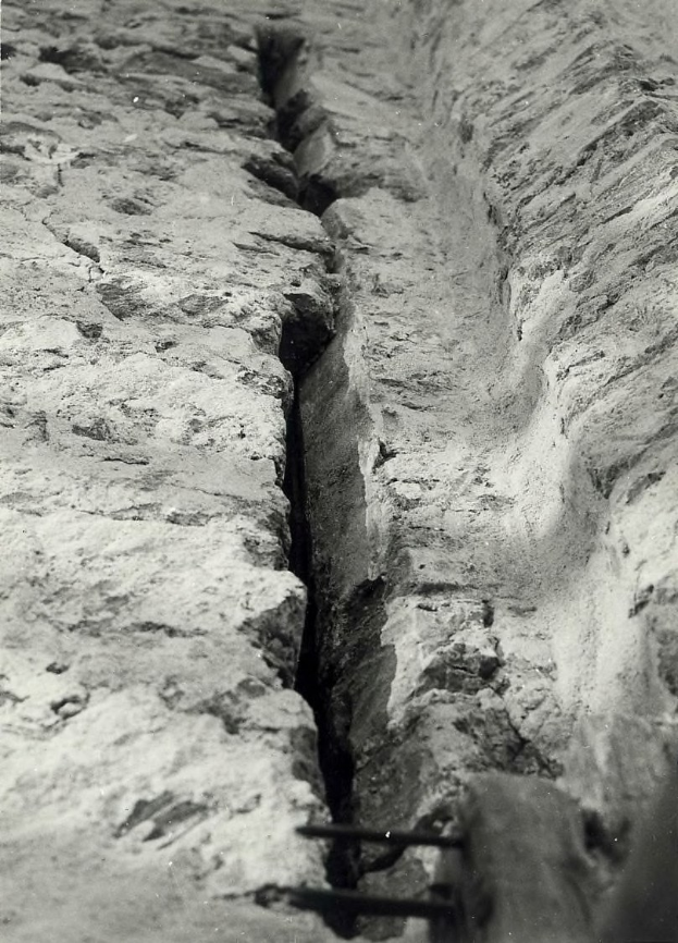 Schwarzes und weißes Foto eines große Risses in einer Bodenentwässerung mit einem Wasserzeichen auf der linken Seite.