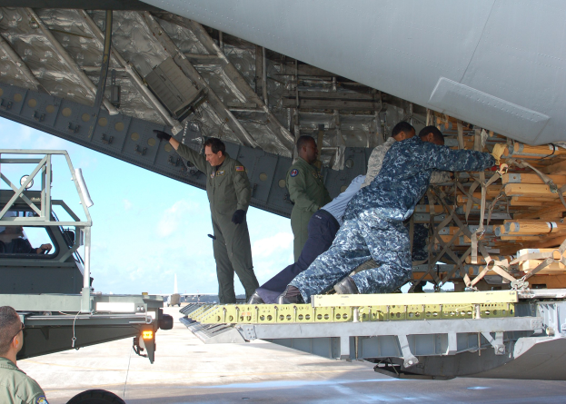 Männer in Uniformen laden ein Cargo-Flugzeug auf einen Lastwagen auf dem Boden mit dem Himmel im Hintergrund.