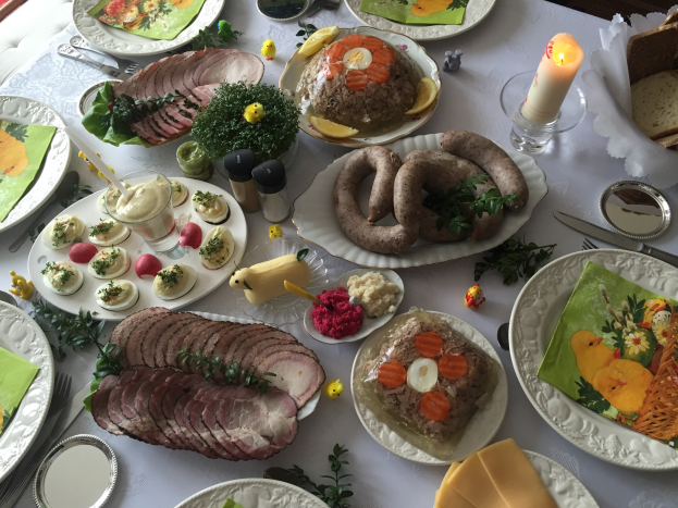 Ein lang gedeckter Tisch mit verschiedenen Gerichten, Besteck, Gläsern, Kerzen und Stühlen, was auf ein traditionelles deutsches Osteressen hinweist.