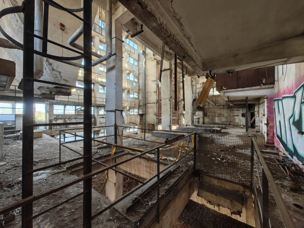 Verlassene Gebäudeinneres mit Graffiti-beschmierten Wänden, bröckelnden Strukturen, Geländern, Pfählen, Rohren und zerbrochenen Fenstern, mit einem Wasserzeichen unten.