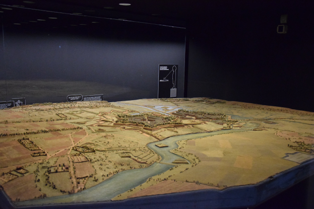 Ein Stadtmodell in einem Museum mit einem Tisch im Vordergrund und einer Texttafel im Hintergrund, unter warmem Deckenlicht.