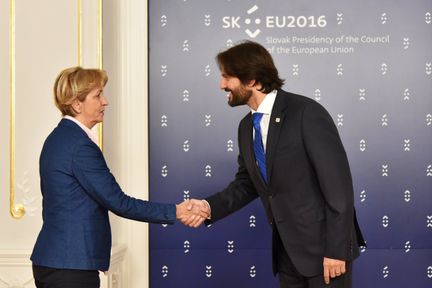 Bundeskanzlerin Angela Merkel und Bundespräsident Joachim Gauck schütteln sich lachend vor einer Wand mit einem "EU-Gipfel"-Schild und einer Tür im Hintergrund die Hand.
