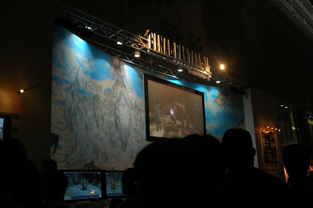 Eine Bühne mit einem Videodisplay in der Mitte, vor der eine Gruppe von Menschen sitzt.