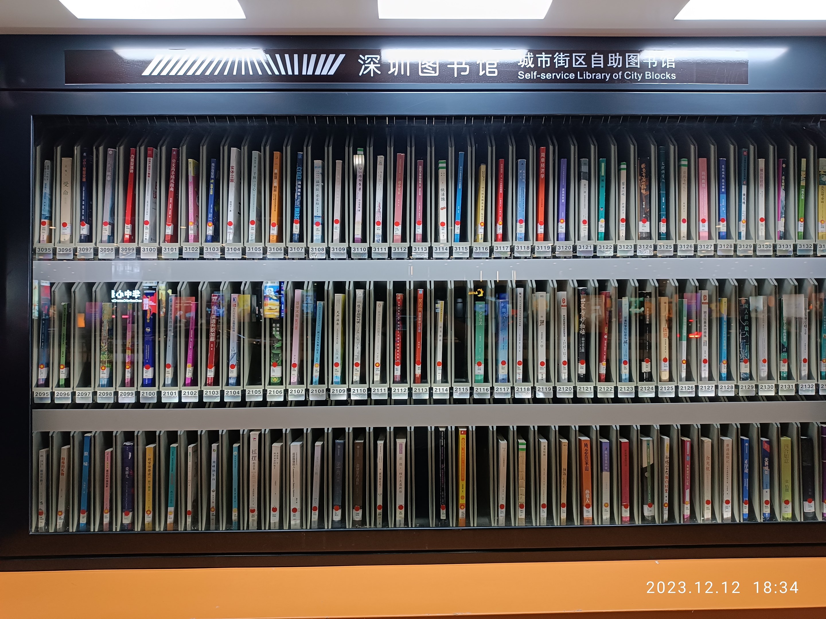 Eine gut beleuchtete Bibliothek mit Bücherregalen, einer Texttafel und einem Wasserzeichen, die an eine Selbstbedienungsbibliothek der Stadtblocks erinnert.