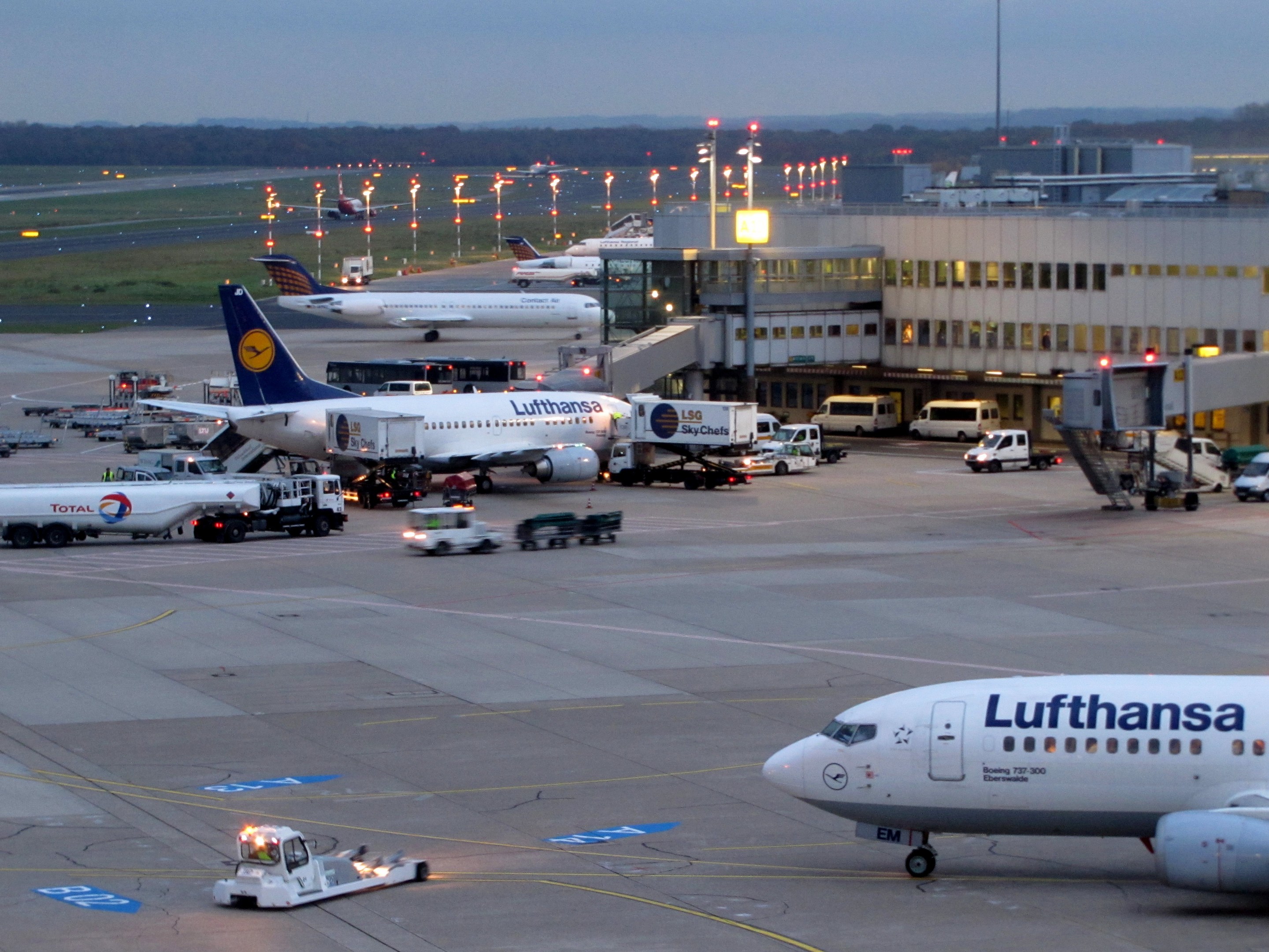 Ein Lufthansa Airbus A330-300 Flugzeuge am Frankfurt Airport geparkt, umgeben von anderen Flugzeugen, Bodenfahrzeugen, Infrastruktur und Vegetation unter einem klaren blauen Himmel.