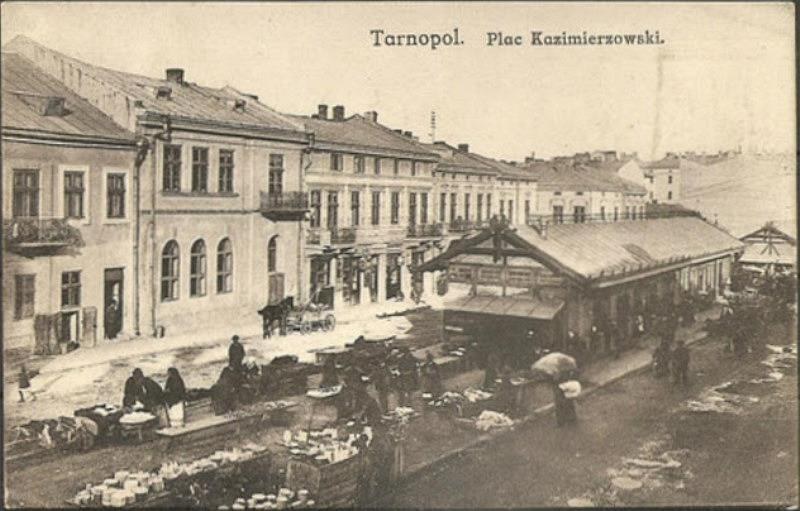 Schwarz-weiß-Foto eines belebten Marktes in Tarnopol, Polen mit Menschen, Karren und Gebäuden im Hintergrund.