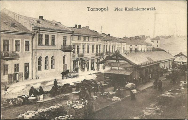 Schwarz-weiß-Foto eines belebten Marktes in Tarnopol, Polen mit Menschen, Karren und Gebäuden im Hintergrund.