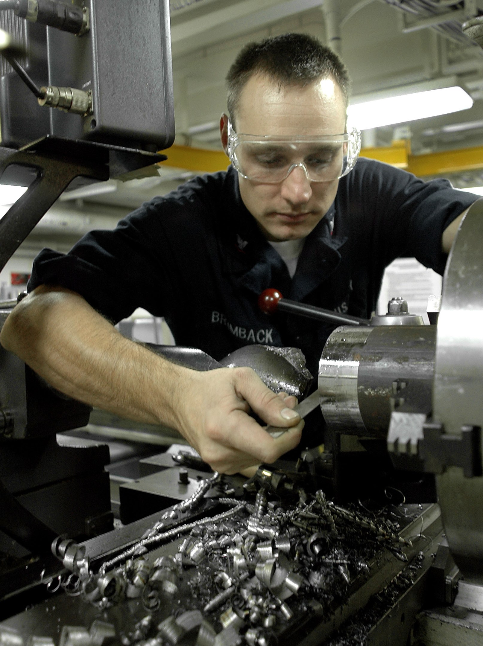 Ein Fräser mit Brille bedient eine Maschine in einer hell erleuchteten Fabrikumgebung.