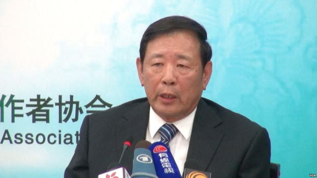 Ein Mann in Anzug und Krawatte sitzt an einem Tisch mit Mikrofonen und spricht hinter einem Banner, wahrscheinlich zu der Nachricht über Chinas Präsident Hu Jintao.