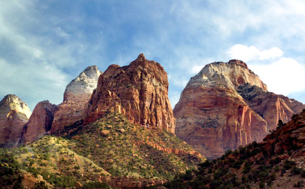 Zion Nationalpark in Utah mit majestätischen Bergen, grünen Bäumen, steinigem Gelände und einem Himmel voller weißer Wolken.