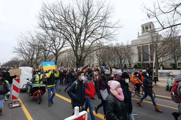 Eine große Gruppe von Menschen marschiert bei einer Demonstration in Washington, D.C. am 21. Januar 2020 mit Schildern, Bannern und Fahrrädern vor einem Gebäude und unter einem klaren blauen Himmel.