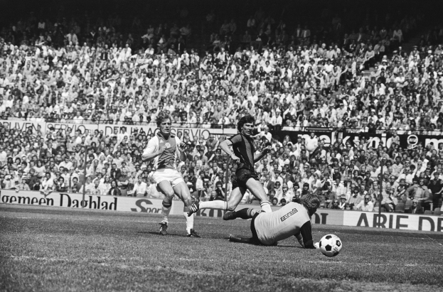 Schwarzes und wei├čes Foto von M├Ąnnern, die auf einem Feld Fussball spielen, mit Zuschauern im Hintergrund und einer Tafel mit der Aufschrift "Bundesliga 1978-79 Ajax 1-1 Hannover 96."