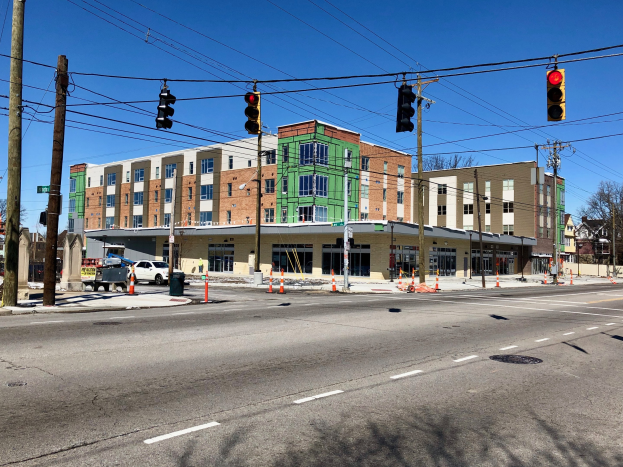 Stadtstraßenszene mit Ampeln, Strommästen, Fahrzeugen, Bäumen, Gebäuden und einer Baustelle im Vordergrund.