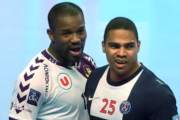 Zwei Männer in weißen und blauen Fußballtrikots stehen nebeneinander auf einem Feld und feiern mit erhobenen Armen.