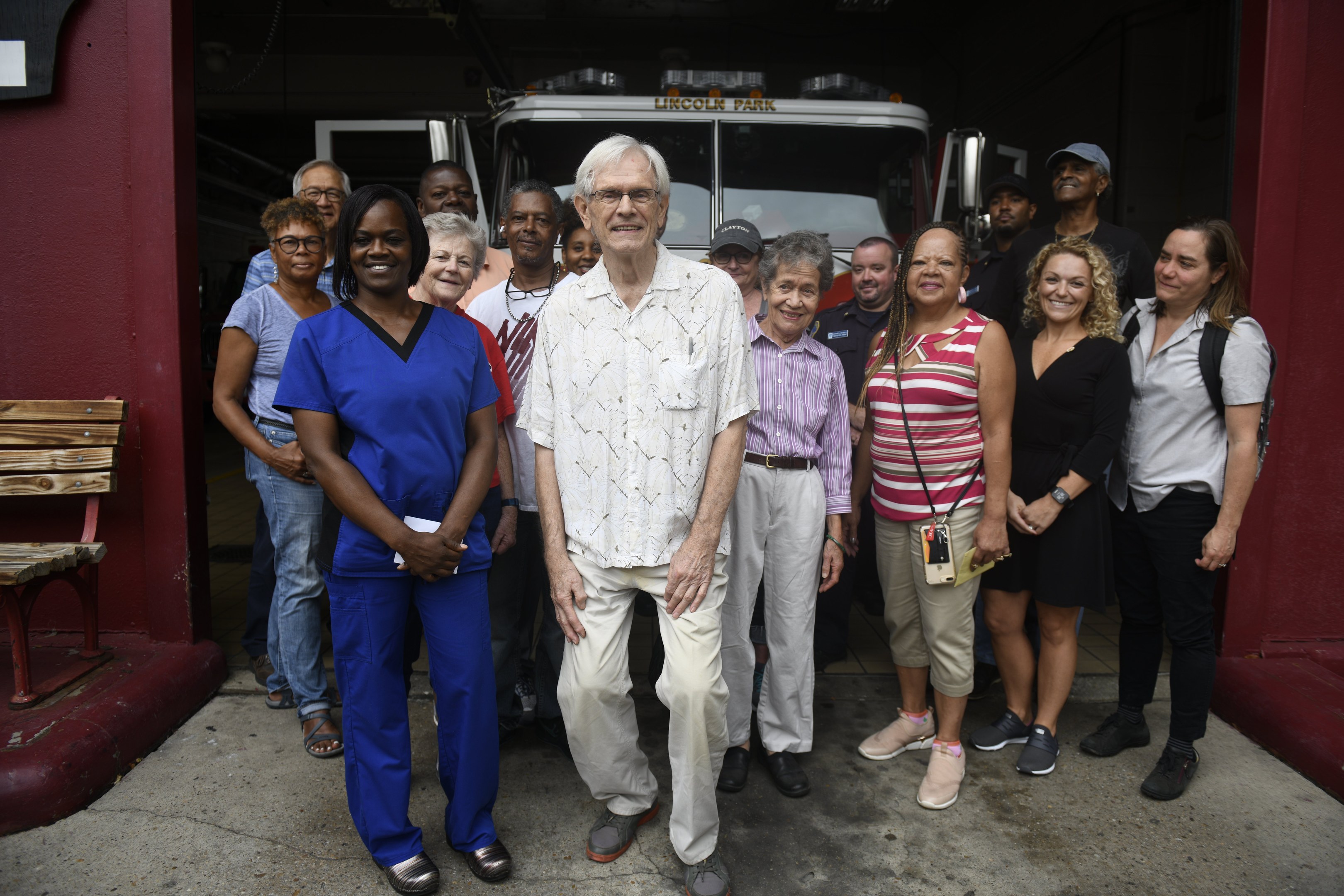 Eine Gruppe von Freiwilligen vor einem Feuerwehrauto, mit einer Bank links und einer Wand im Hintergrund.