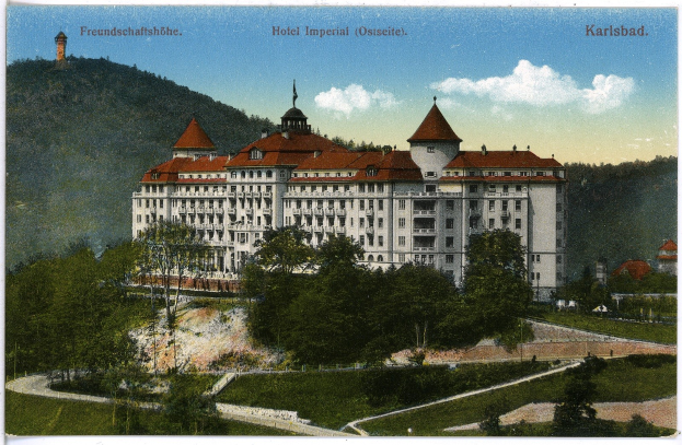 Alte Ansichtskarte des Hotels Imperial in Karlsbad, Deutschland, zeigt ein großes Gebäude mit Fenstern, umgeben von Bäumen, Pflanzen, Gras, einem Weg, einer Baumgruppe, Hügeln und einem bewölkten Himmel, mit Text oben.