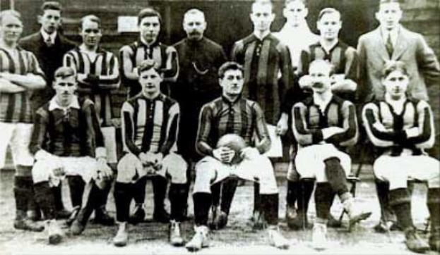 Schwarzes und weißes Foto einer Fußballmannschaft, einige stehen, einige sitzen, vor einer Wand mit der Aufschrift "Ballymena Football Club" unten.