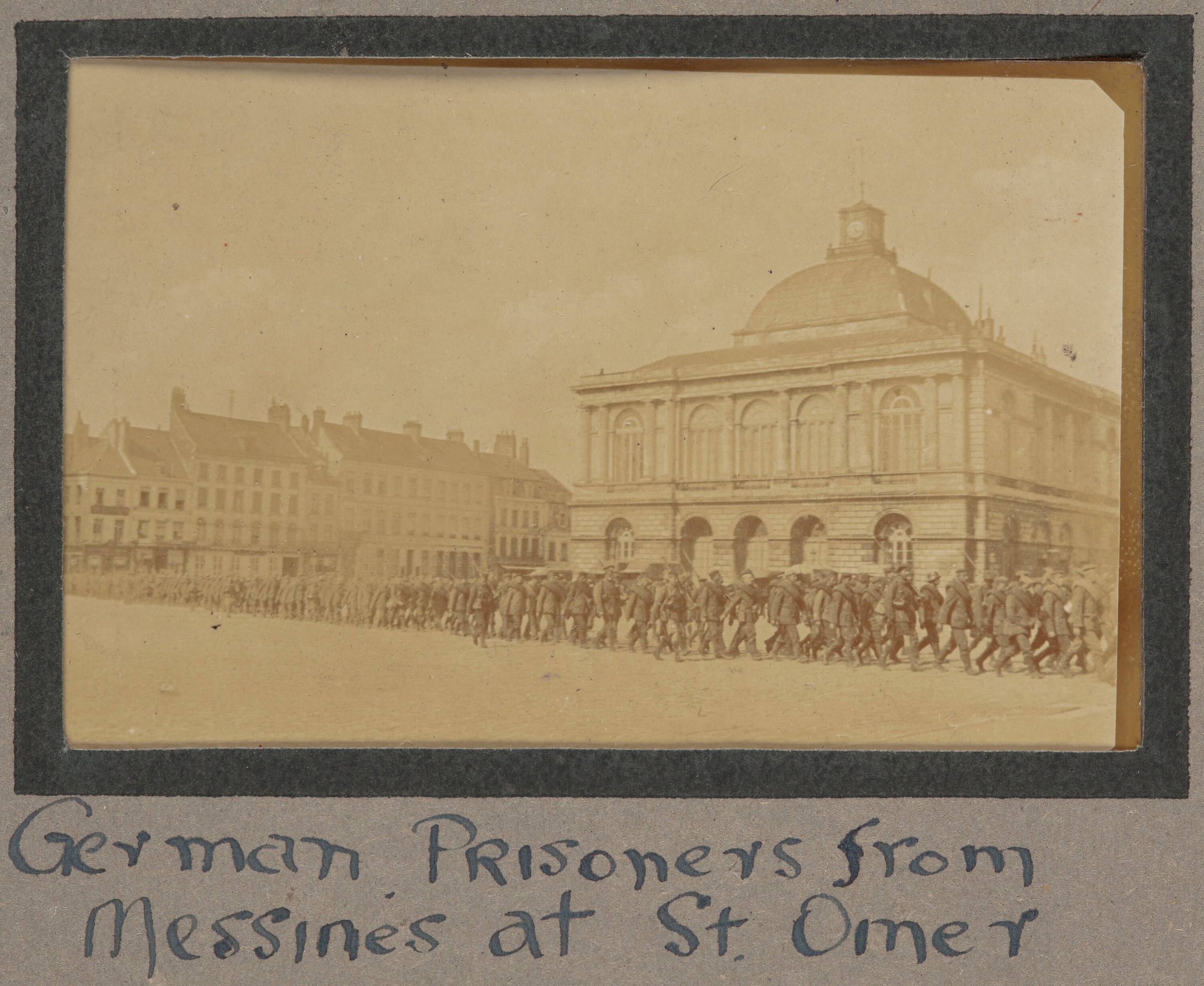 Deutsche Gefangene aus Messines vor einem Gebäude mit Text unten unter einem klaren blauen Himmel.