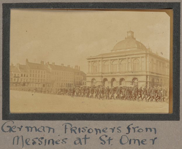Deutsche Gefangene aus Messines vor einem Gebäude mit Text unten unter einem klaren blauen Himmel.