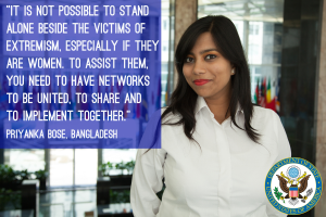 Eine Frau in einem weißen Hemd steht vor einem Gebäude mit einer Aussage über die Einheit gegen Extremismus, ein Logo in der unteren rechten Ecke.