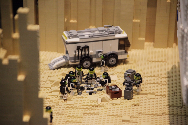 Lego-Modell einer Star-Wars-Szene mit einem Bodenfahrzeug im Vordergrund und einer Wand im Hintergrund, umgeben von verstreuten Lego-Spielzeugen.