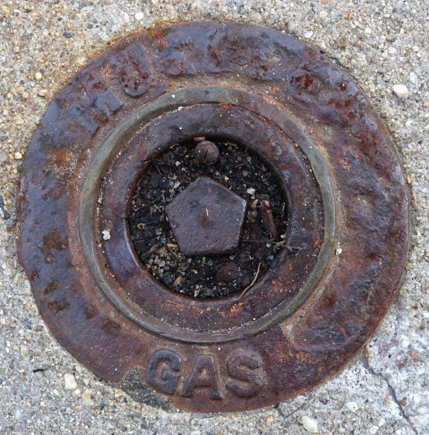 Rostiger Metall-Schachtobel auf dem Boden mit dem Wort "Gas" darauf.